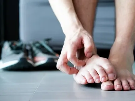 Stock photograph of a model: a person sitting on the floor scratches between the toes of a bare foot