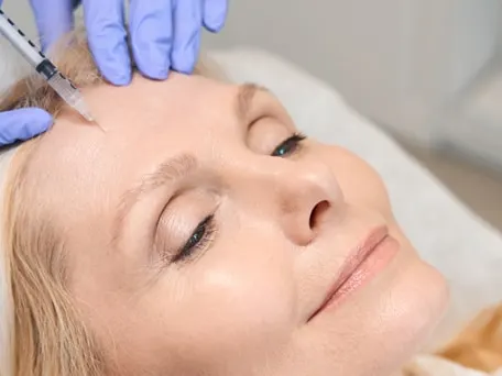 Stock photograph of models: a woman lies back with her eyes closed while a gloved clinician injects her forehead