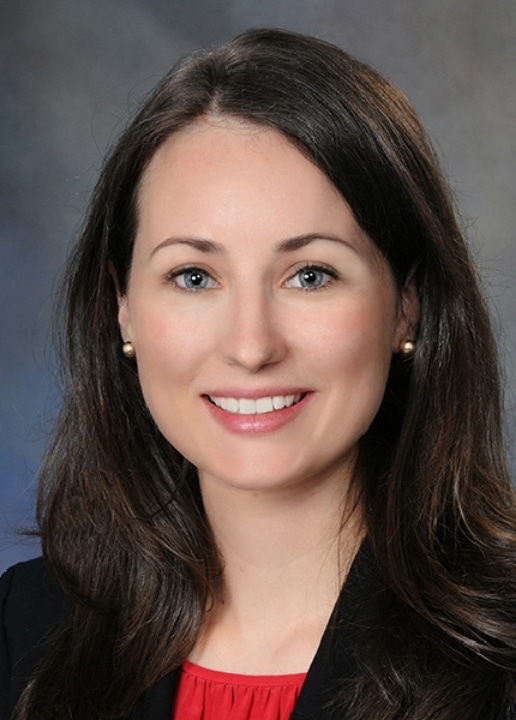 Portrait of Dr. Megan Trainor, MD, FAAD, smiling, in a black blazer
