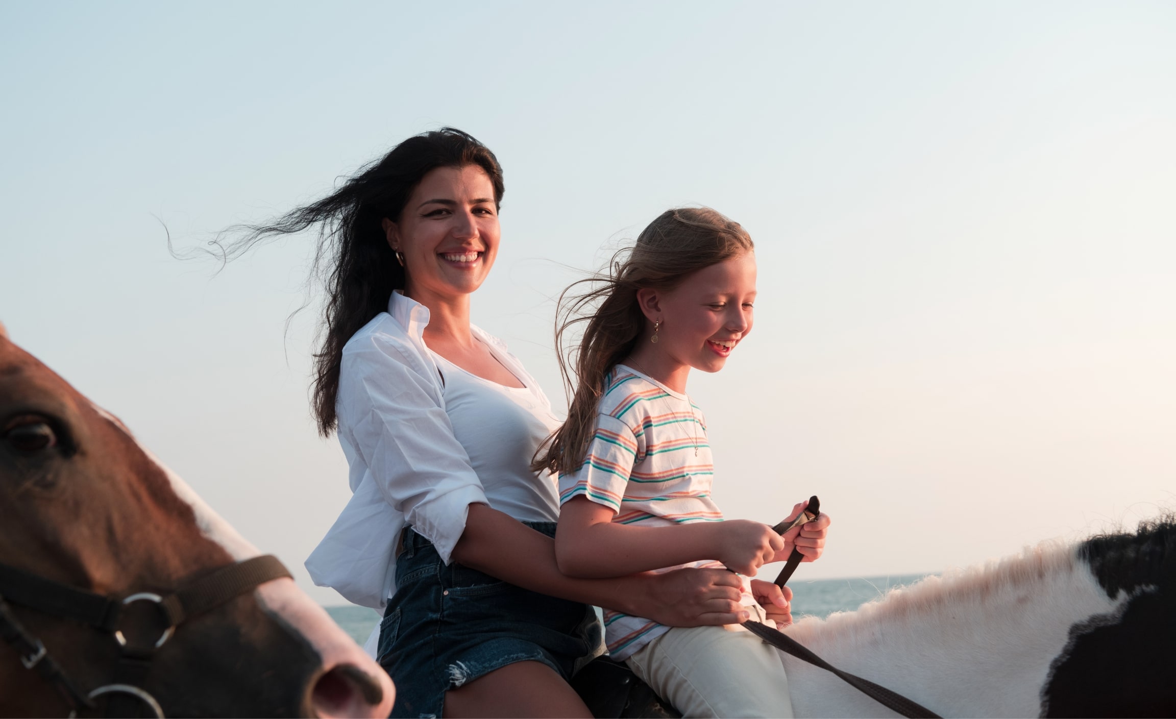 Stock photograph of models: a smiling mother and daughter riding a horse on a beach
