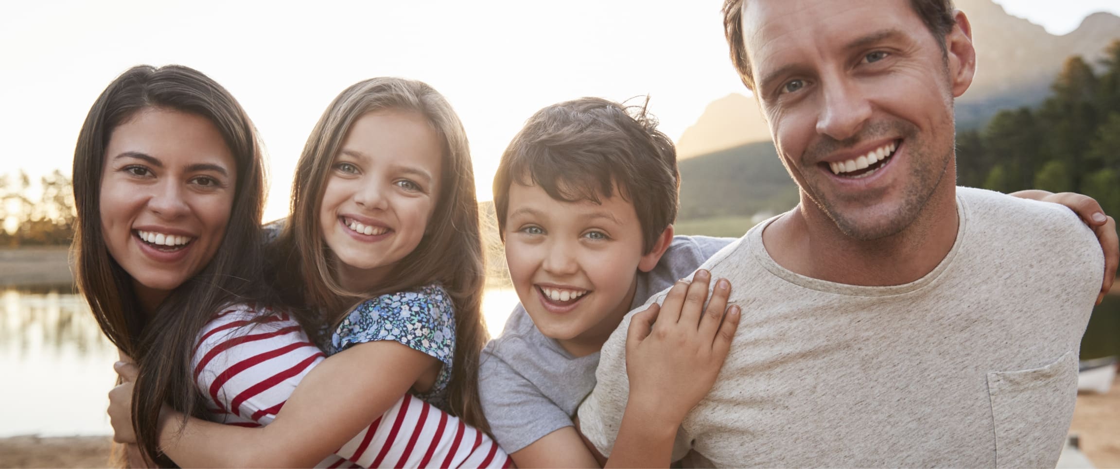 Stock photograph of models: a smiling family of four hugging outdoors by a lake