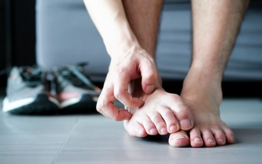 Stock photograph of a model: a person sitting on the floor scratches between the toes of a bare foot